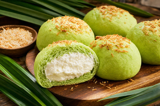 Freshly baked pandan coconut buns split open to reveal whipped cream filling, topped with toasted coconut flakes