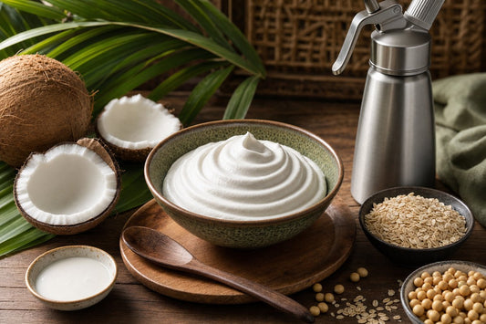Vegan whipped cream with coconut, oat, and soy ingredients next to a cream dispenser on a wooden table