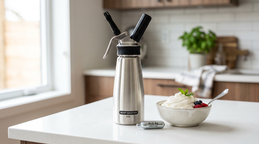Stainless steel cream dispenser with N2O charger and bowl of whipped cream on a kitchen counter